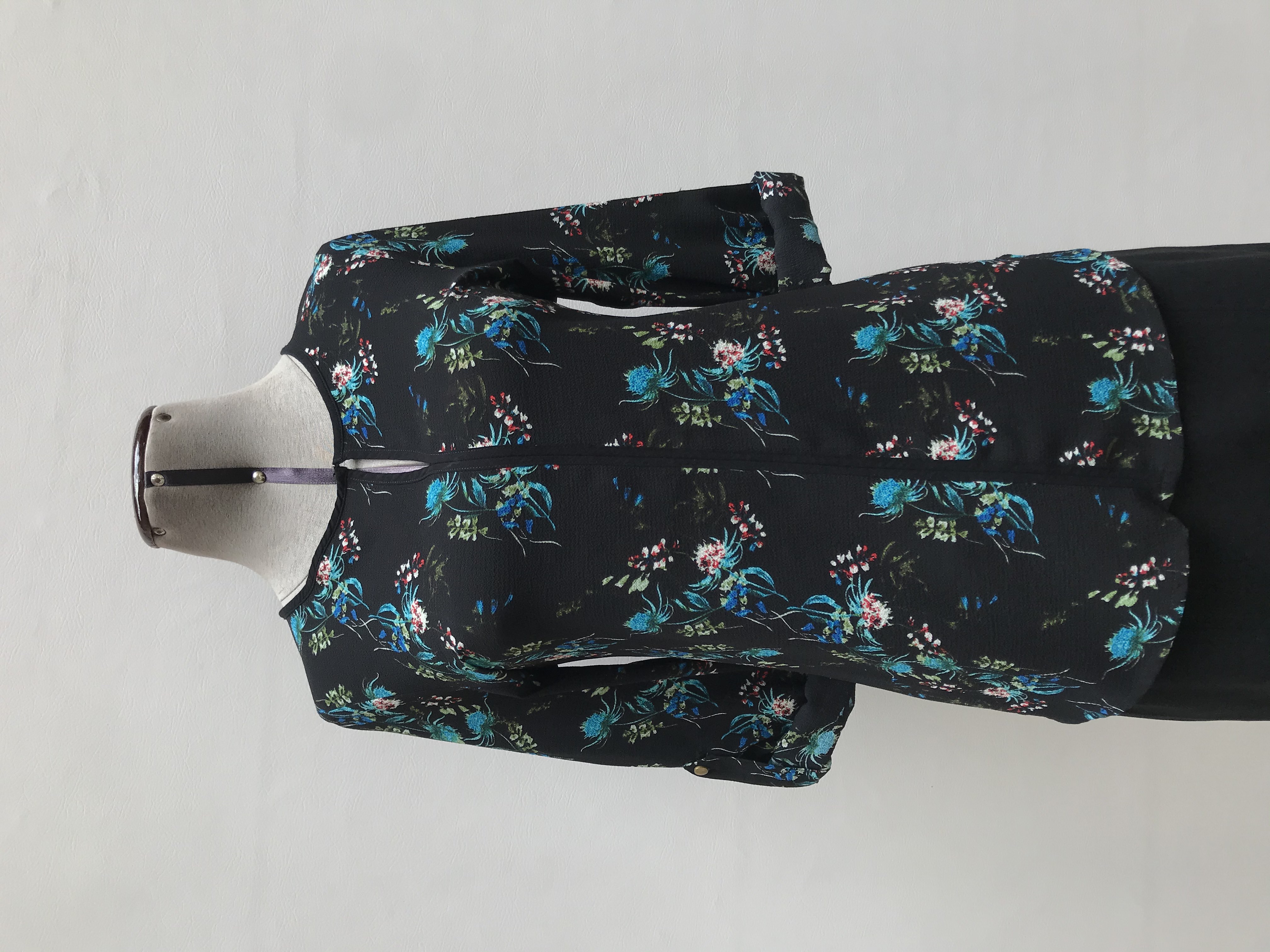 Blusa Cacharel tipo gasa gruesa negra con estampado de flores en tonos azules, escote gota con franja negra en el medio y mangas regulables con botón
Talla S